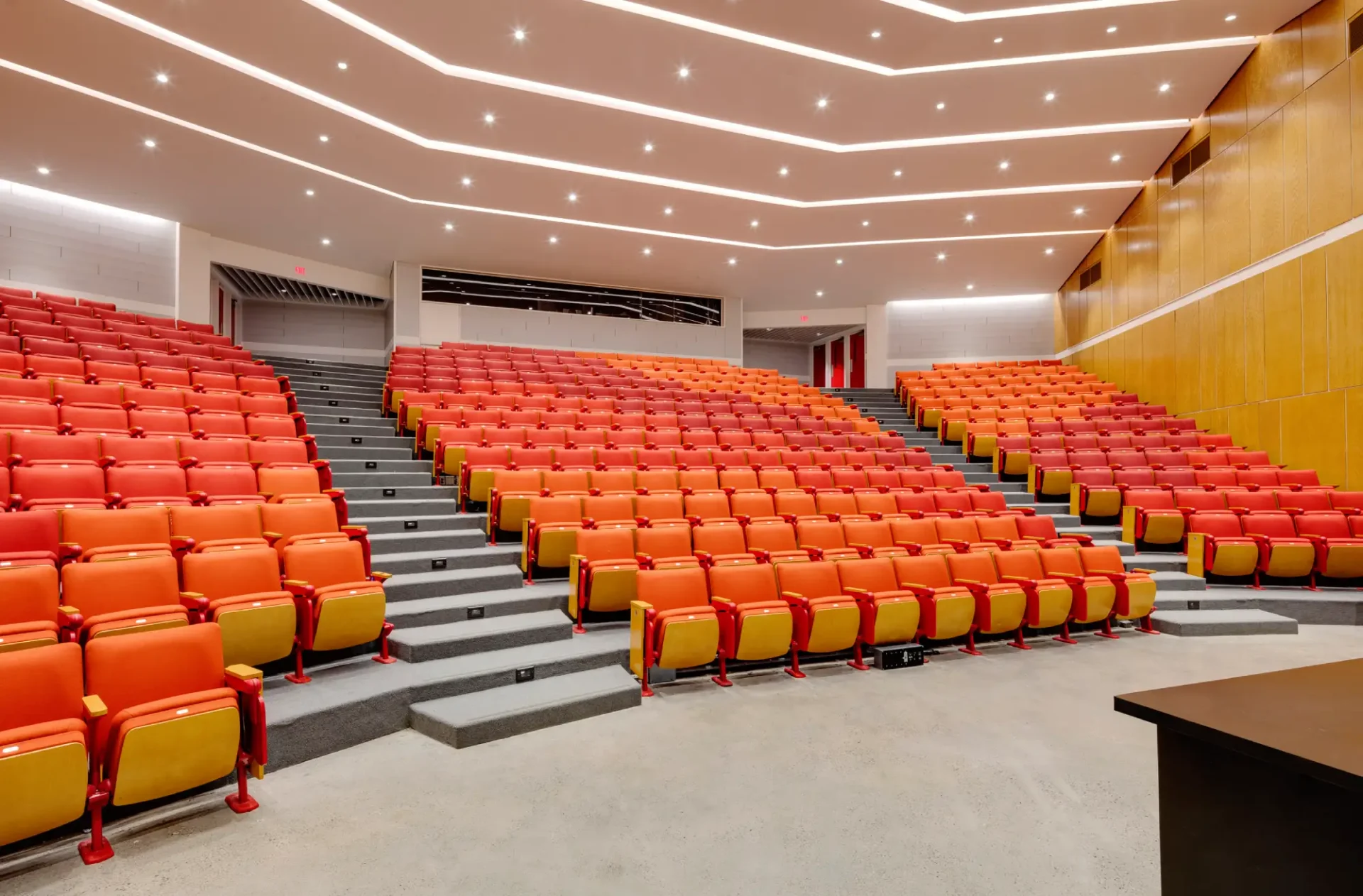 A large auditorium with orange seats and yellow chairs.