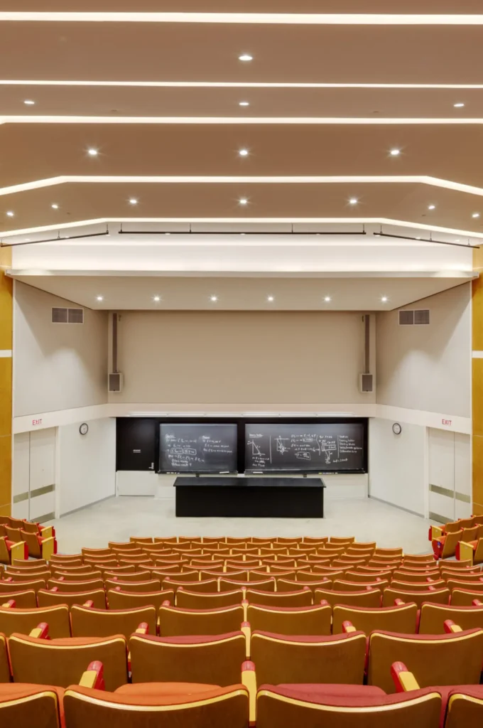 A large auditorium with two big screens and rows of seats.