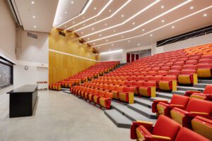 A large auditorium with red seats and yellow chairs.